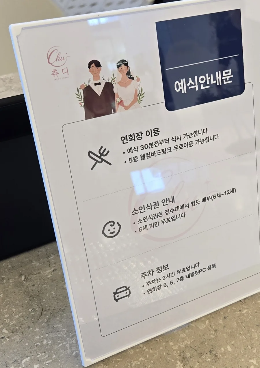 축의대 위 아크릴 거치대에 세운 예식안내문. 연회장 이용, 소인식권, 주차 정보를 안내한다