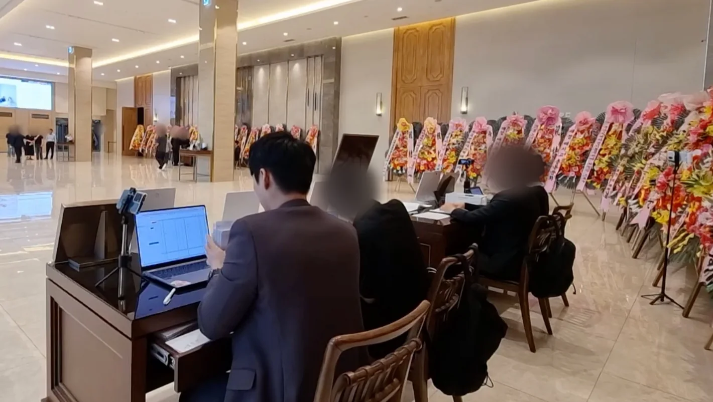 화환이 늘어선 로비에서 매니저 셋이 노트북으로 축의 내역을 입력하는 모습